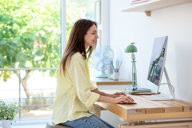 Photo of Woman using computer at wooden desk indoors. Home workplace