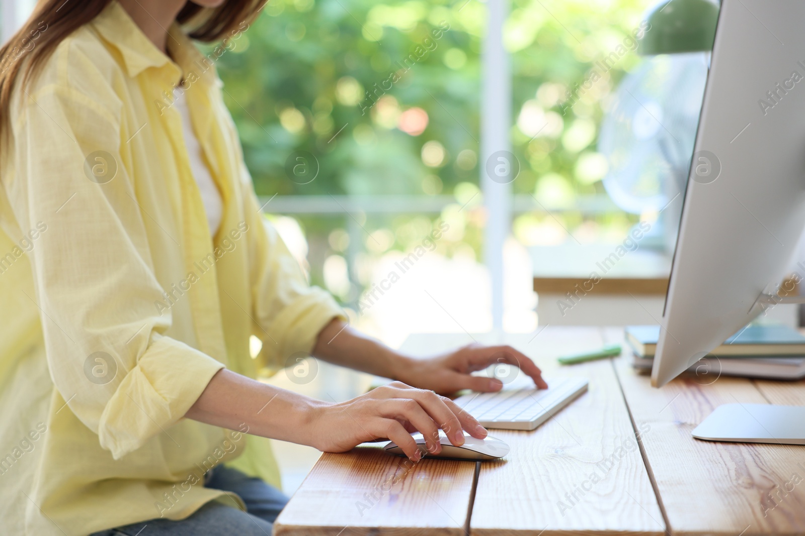 Photo of Woman using computer at wooden desk indoors, closeup. Home workplace