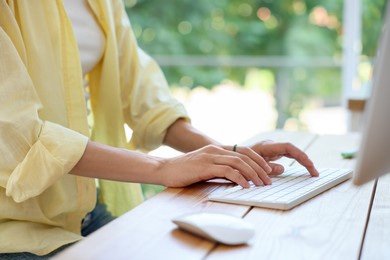Photo of Woman using computer at wooden desk indoors, closeup. Home workplace
