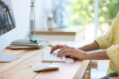 Photo of Woman using computer at wooden desk indoors, closeup. Home workplace