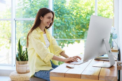 Photo of Woman using computer at wooden desk indoors. Home workplace