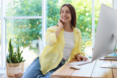 Photo of Woman using computer at wooden desk indoors. Home workplace
