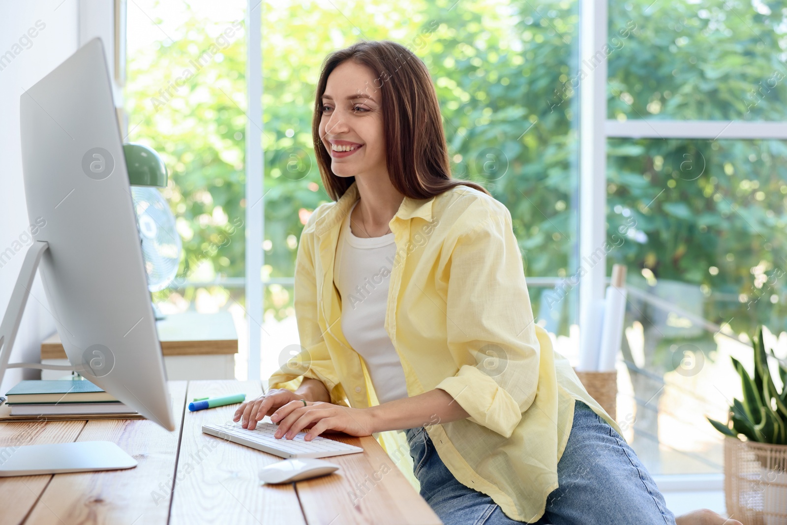 Photo of Woman using computer at wooden desk indoors. Home workplace