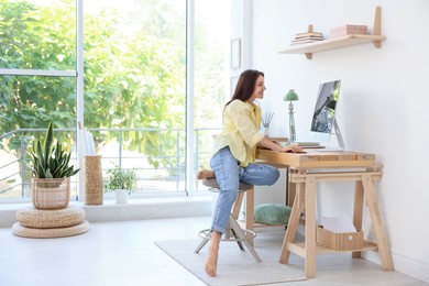 Photo of Woman using computer at wooden desk indoors, space for text. Home workplace
