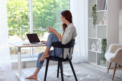Photo of Woman with coffee at wooden desk indoors. Home workplace
