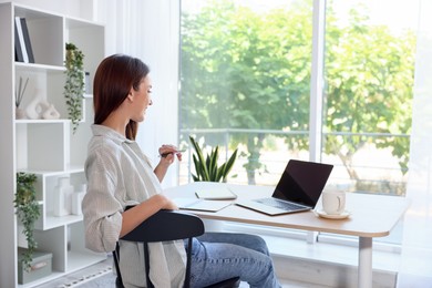 Photo of Woman at wooden desk indoors, back view. Home workplace