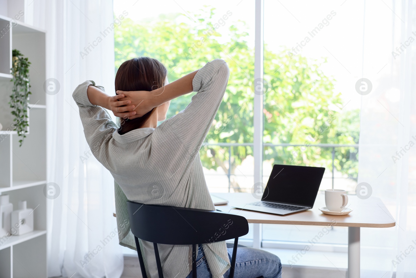 Photo of Woman at wooden desk indoors, back view. Home workplace