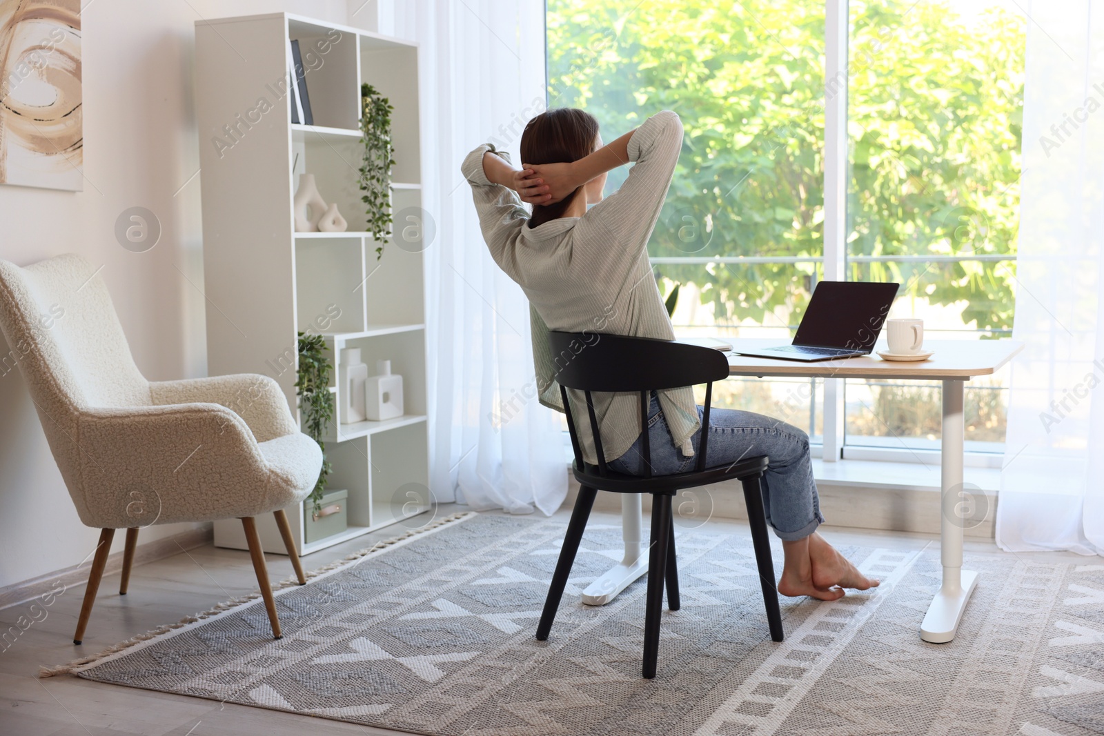 Photo of Woman at wooden desk indoors, back view. Home workplace