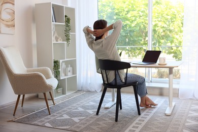 Photo of Woman at wooden desk indoors, back view. Home workplace