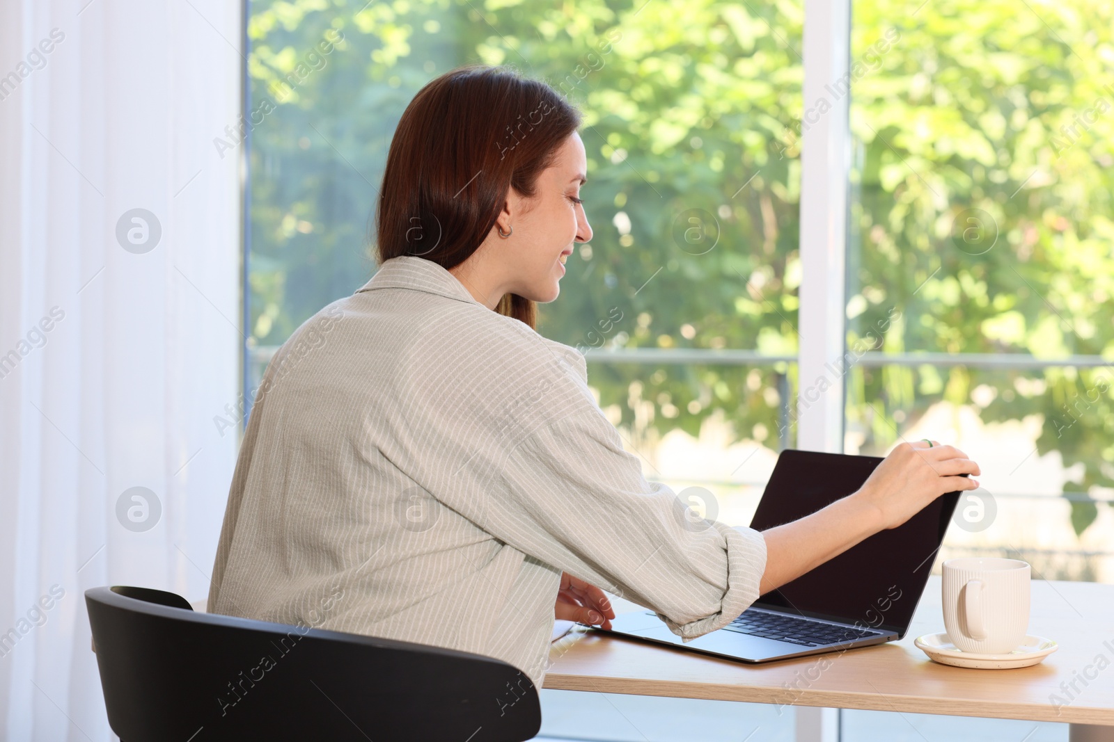 Photo of Woman using laptop at wooden desk indoors. Home workplace