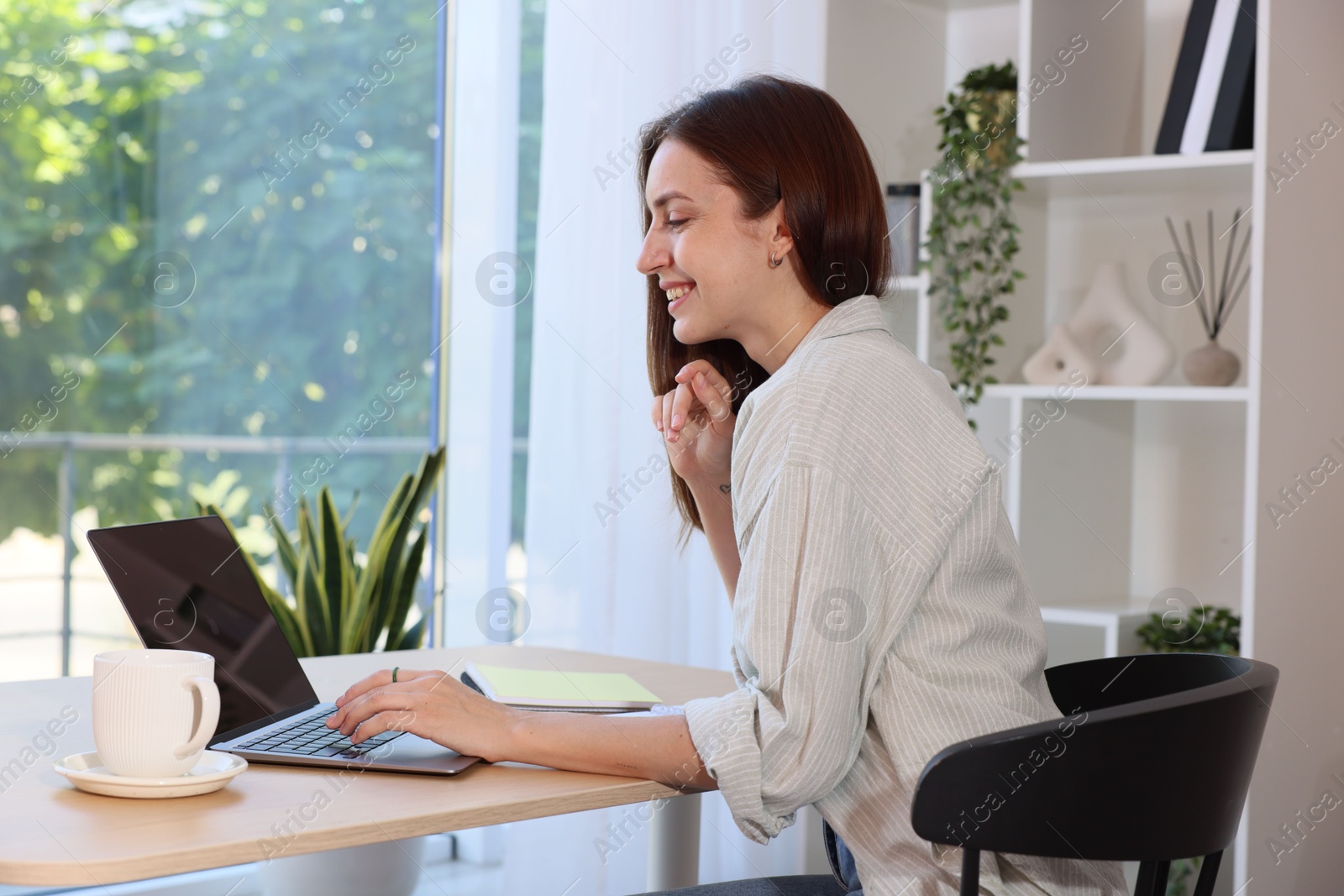 Photo of Woman using laptop at wooden desk indoors. Home workplace