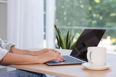 Photo of Woman using computer at wooden desk indoors, closeup. Home workplace