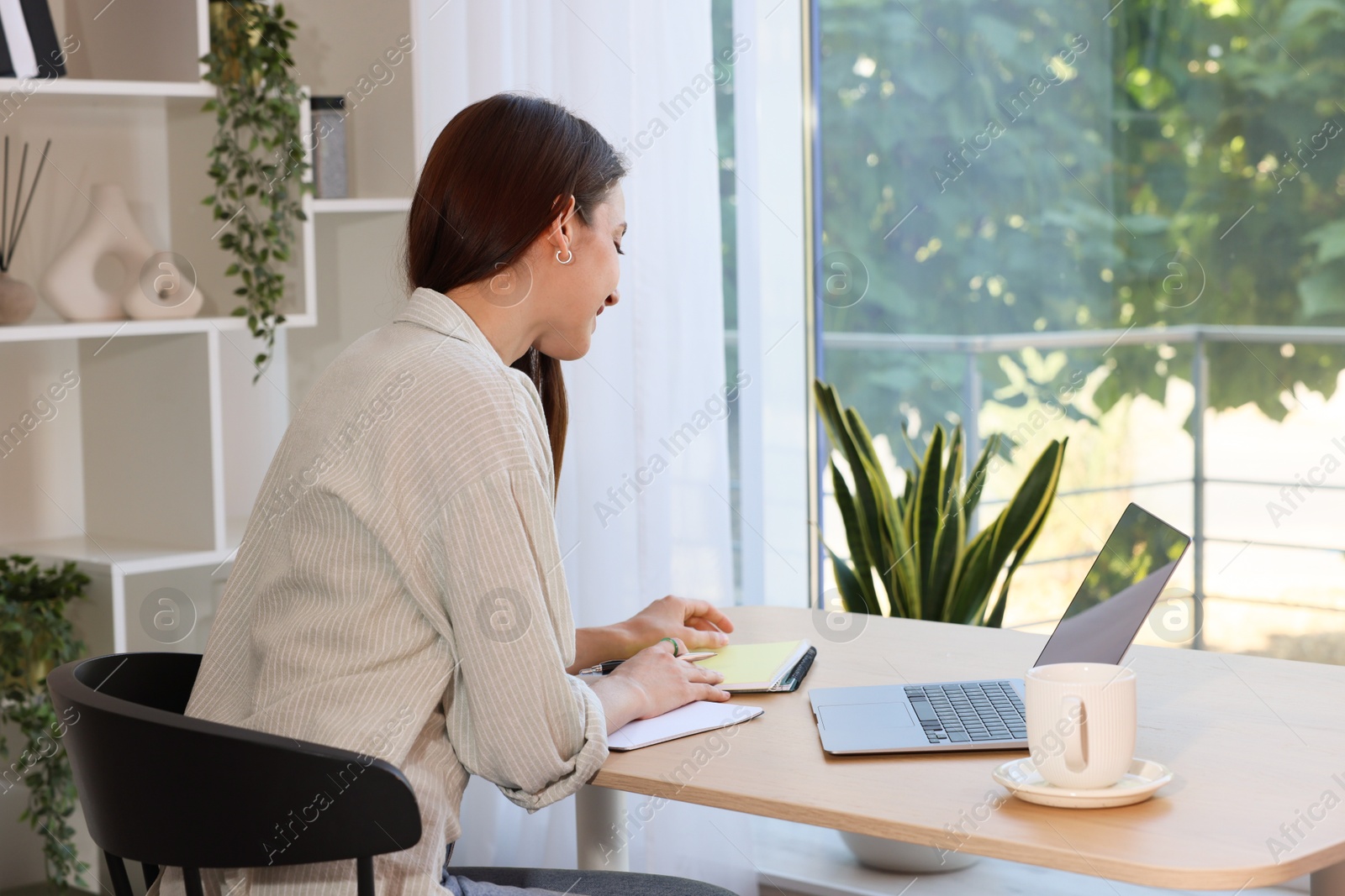 Photo of Woman using laptop at wooden desk indoors. Home workplace