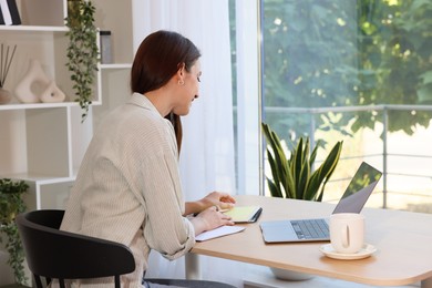 Photo of Woman using laptop at wooden desk indoors. Home workplace