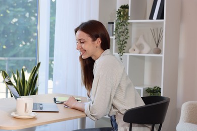 Photo of Woman using laptop at wooden desk indoors. Home workplace