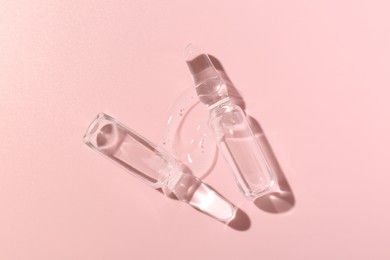 Photo of Glass ampoules with cosmetic product on pink background, flat lay