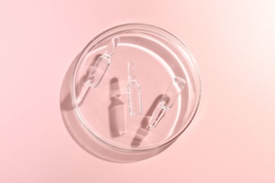 Photo of Glass ampoules with cosmetic product and Petri dish on pink background, top view