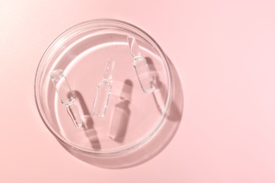 Photo of Glass ampoules with cosmetic product and Petri dish on pink background, top view