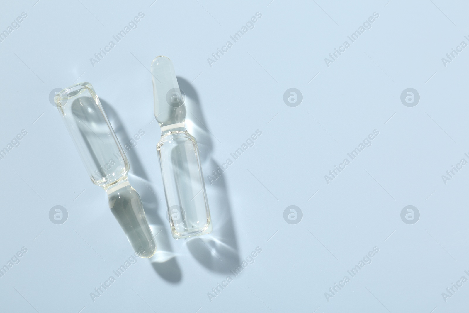 Glass ampoules with cosmetic product on light blue background, flat lay. Space for text Photo of Glass ampoules with cosmetic product on light blue background, flat lay. Space for text