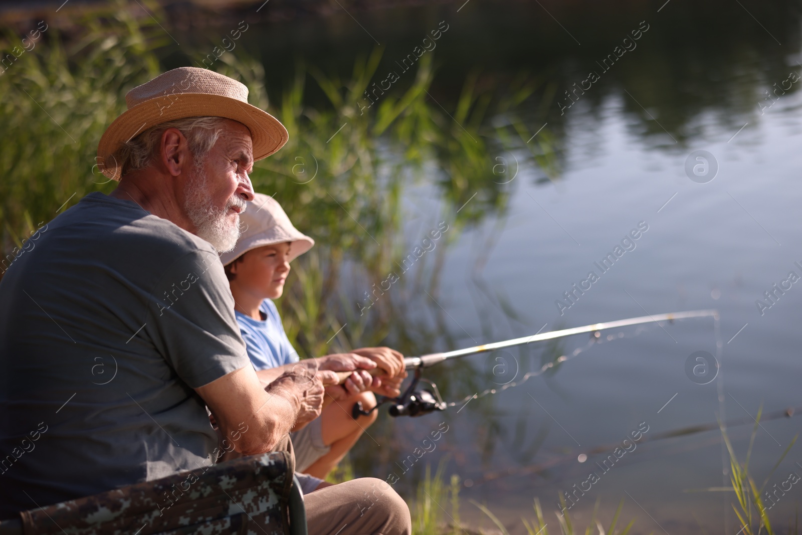 Grandfather and his nephew fishing together near river outdoors Photo of Grandfather and his nephew fishing together near river outdoors