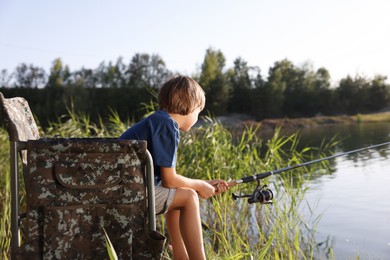 Photo of Little boy sitting on folding chair and fishing near river outdoors