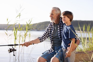 Photo of Smiling grandfather and his nephew fishing together near river outdoors