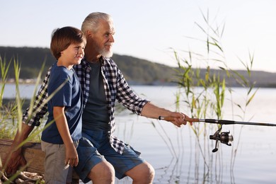 Photo of Smiling grandfather and his nephew fishing together near river outdoors