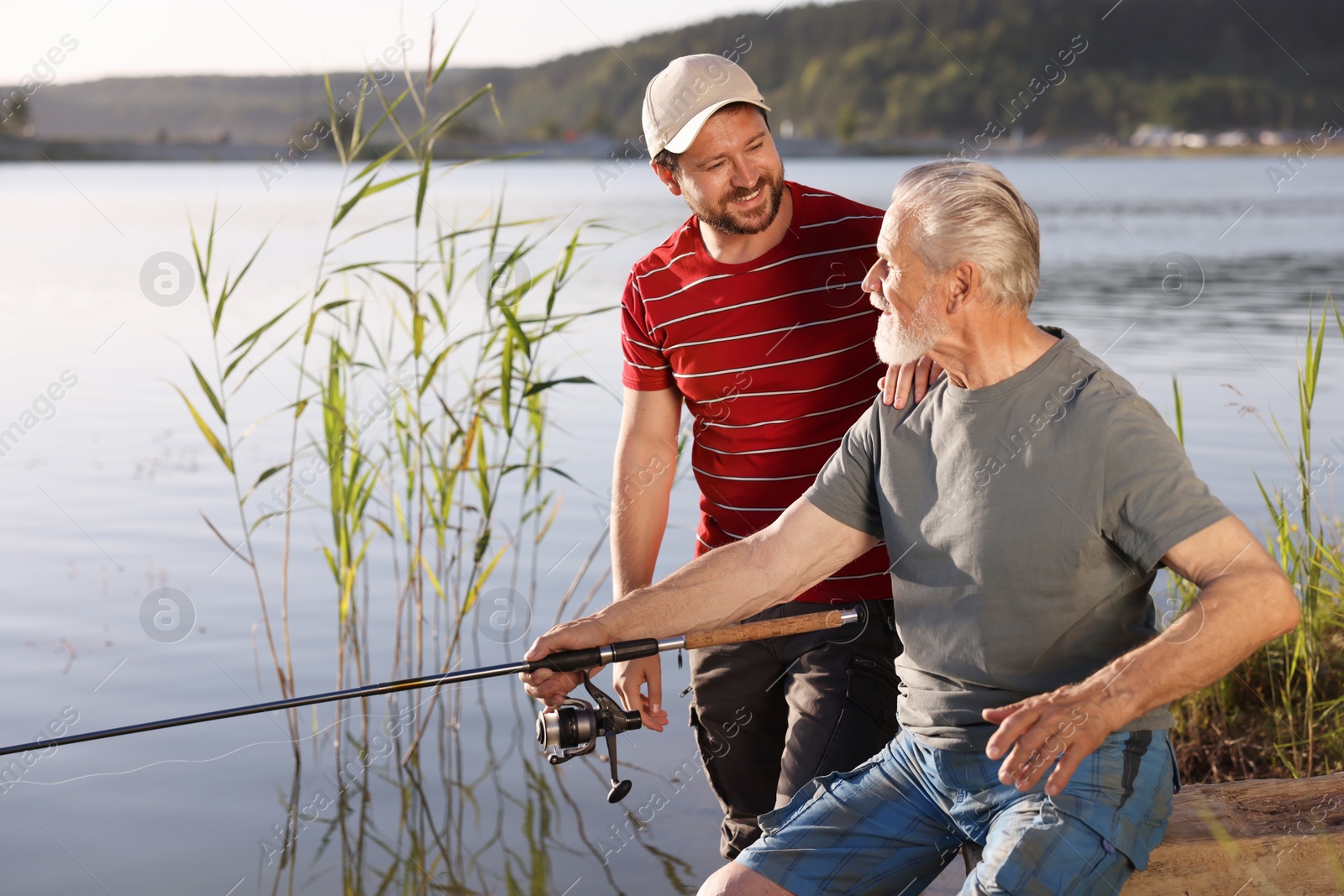 Elderly father and his happy son fishing together near river outdoors Photo of Elderly father and his happy son fishing together near river outdoors