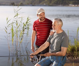 Photo of Elderly father and his happy son fishing together near river outdoors