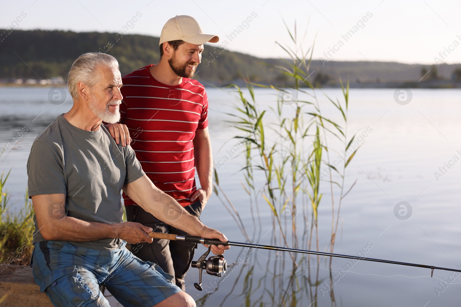 Elderly father and his happy son fishing together near river outdoors Photo of Elderly father and his happy son fishing together near river outdoors