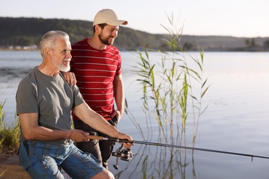 Photo of Elderly father and his happy son fishing together near river outdoors
