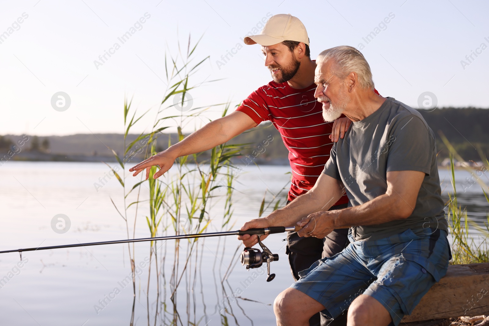 Elderly father and his happy son fishing together near river outdoors Photo of Elderly father and his happy son fishing together near river outdoors