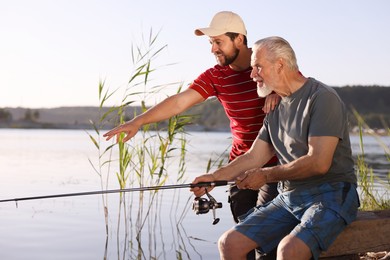 Photo of Elderly father and his happy son fishing together near river outdoors