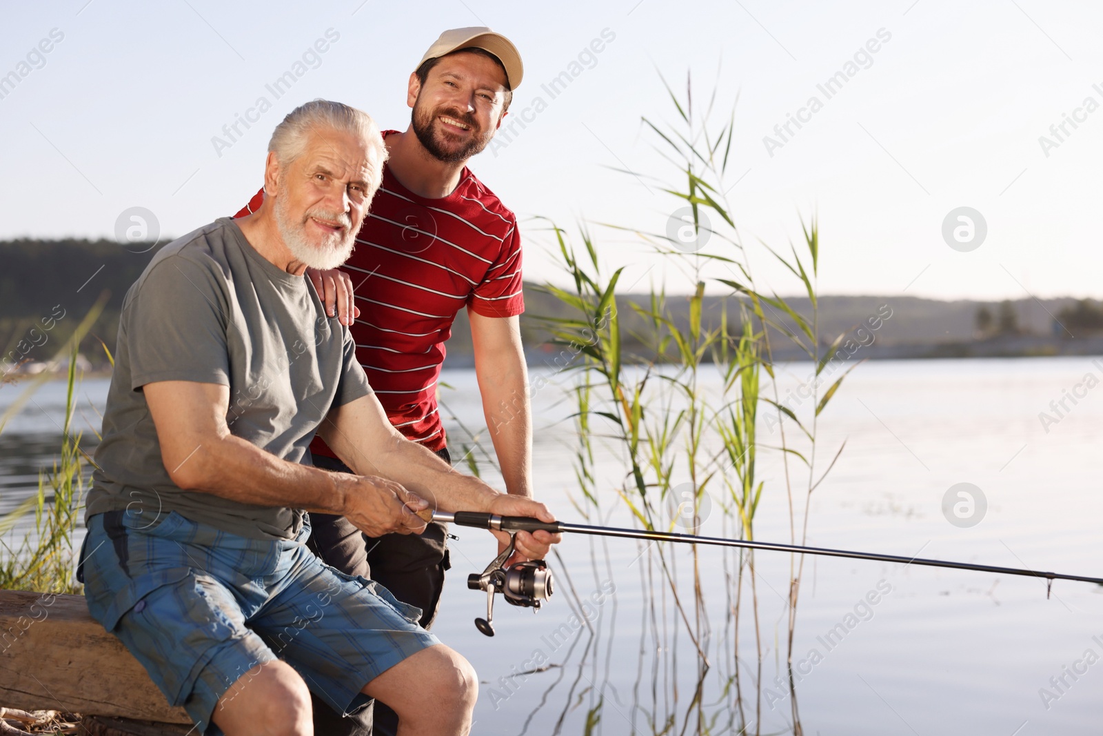 Photo of Elderly father and his happy son fishing together near river outdoors