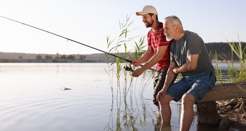 Photo of Elderly father and his happy son fishing together in river outdoors