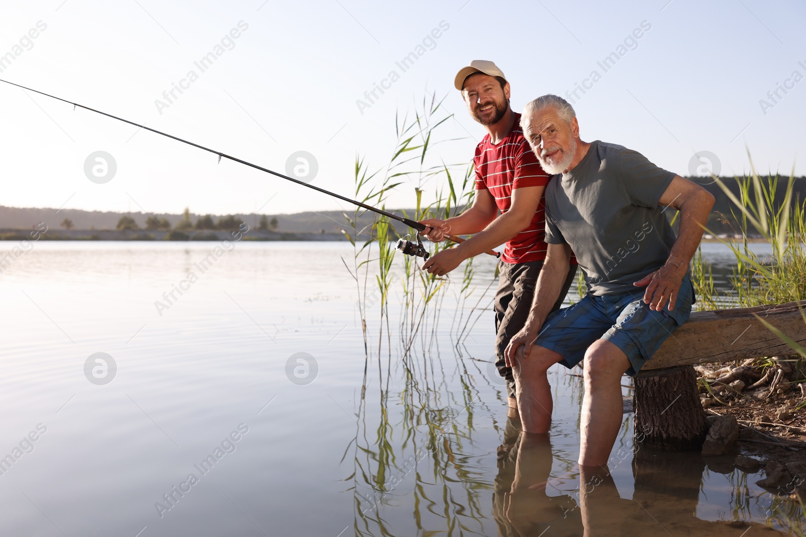 Photo of Elderly father and his happy son fishing together in river outdoors