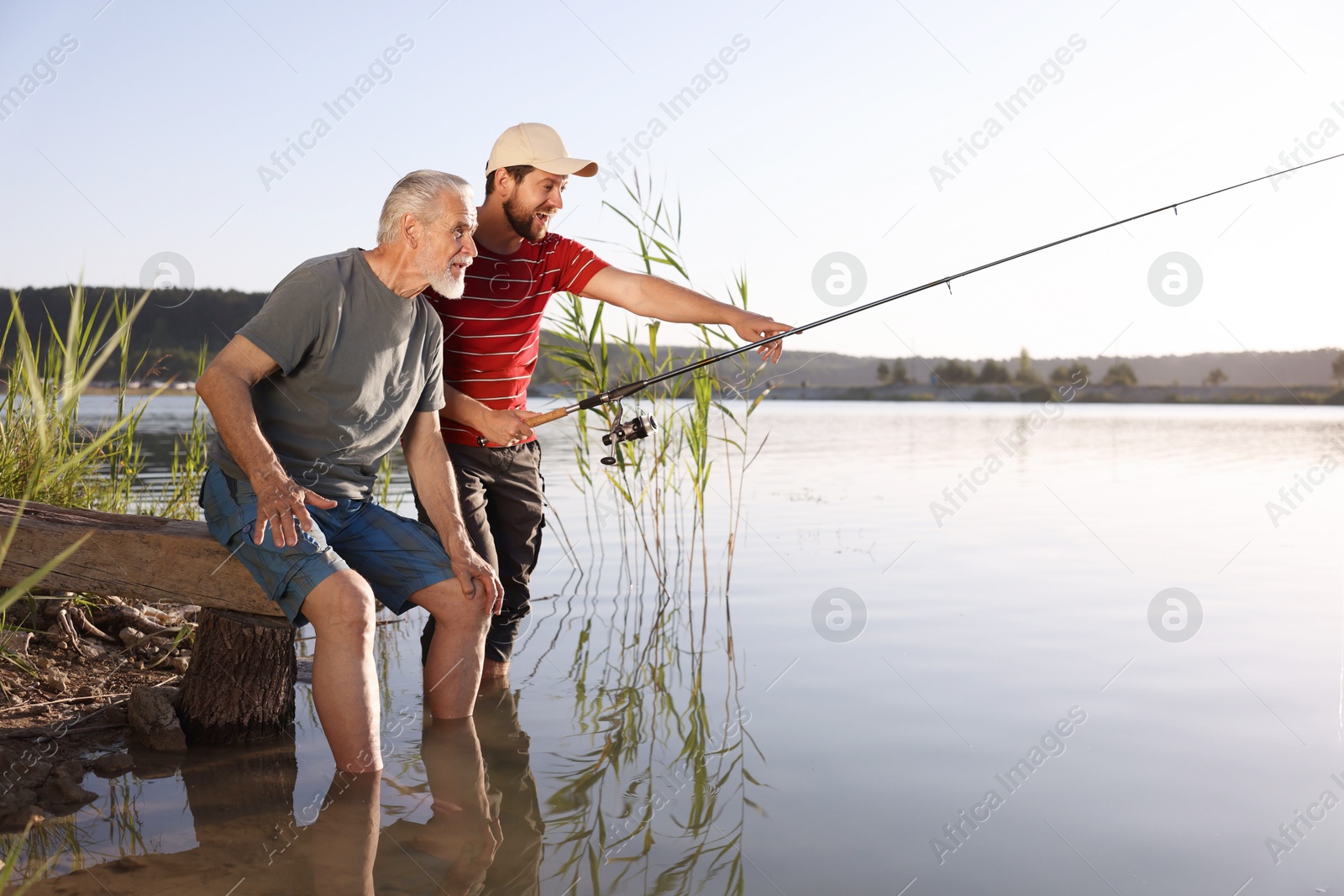 Elderly father and his happy son fishing together in river outdoors Photo of Elderly father and his happy son fishing together in river outdoors