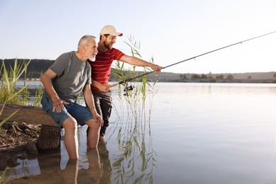 Photo of Elderly father and his happy son fishing together in river outdoors