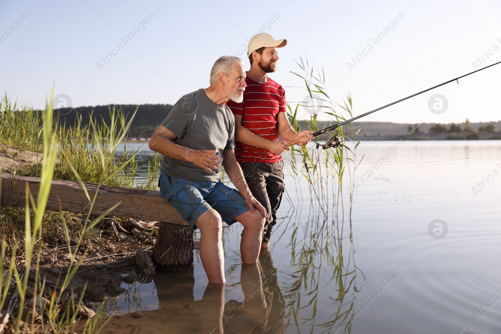 Elderly father and his happy son fishing together in river outdoors Photo of Elderly father and his happy son fishing together in river outdoors