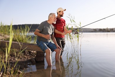 Photo of Elderly father and his happy son fishing together in river outdoors
