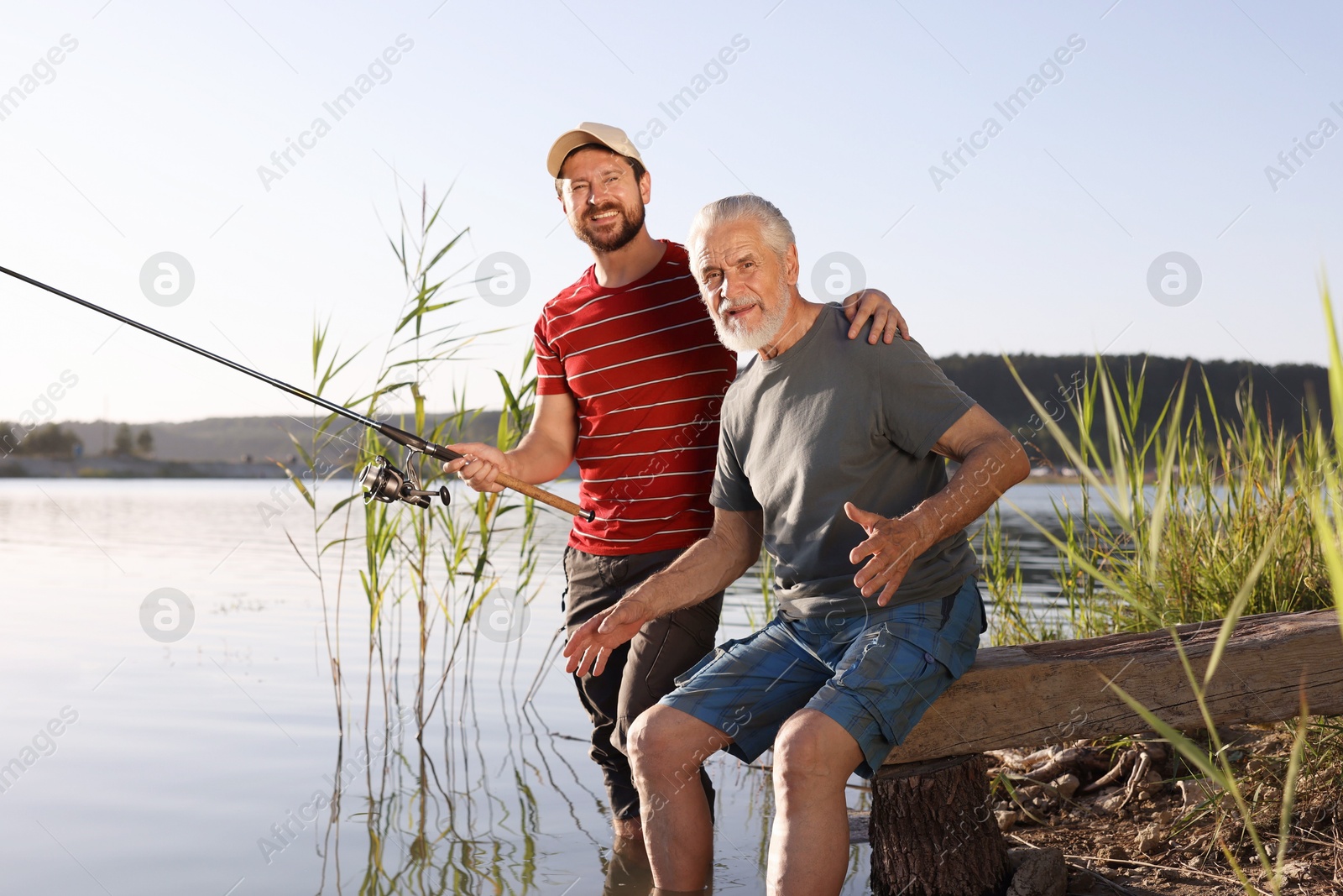 Photo of Elderly father and his happy son fishing together in river outdoors