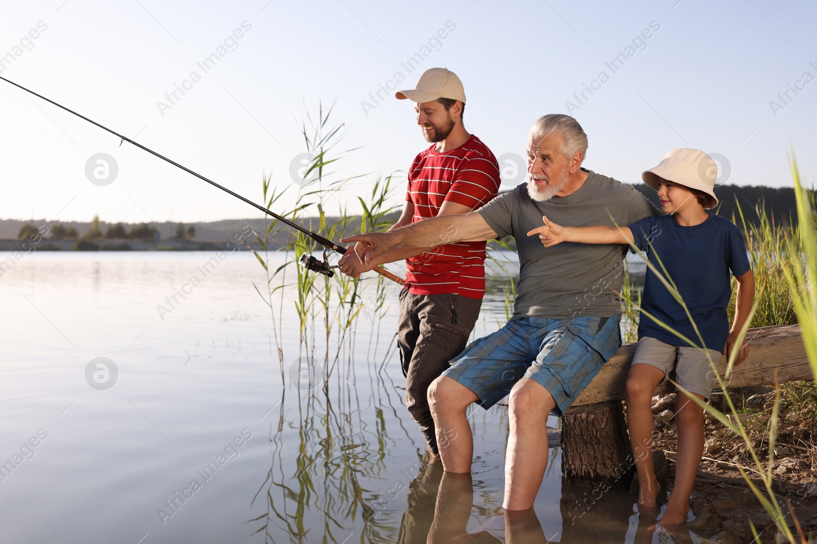 Photo of Grandfather, father and his little son fishing together in river outdoors