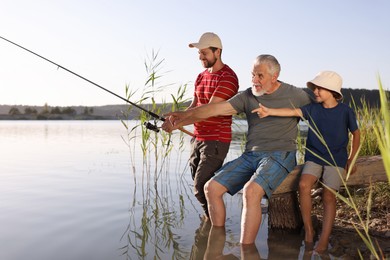 Photo of Grandfather, father and his little son fishing together in river outdoors