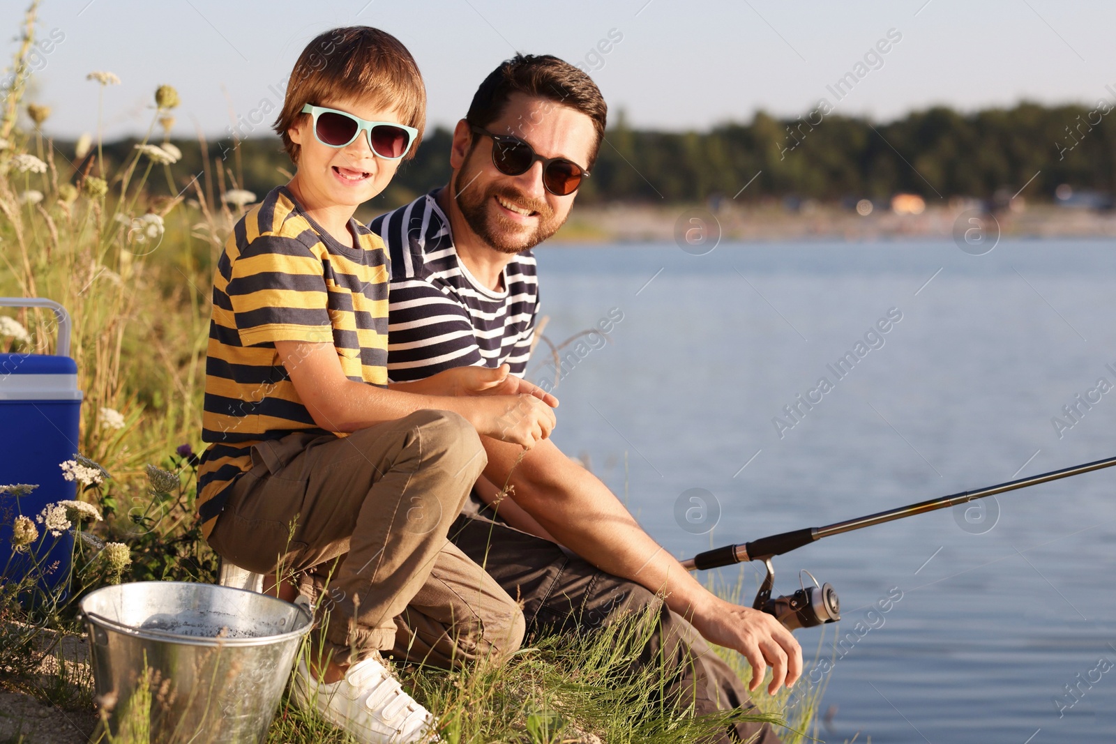 Happy father and his little son in sunglasses fishing together near river outdoors Photo of Happy father and his little son in sunglasses fishing together near river outdoors