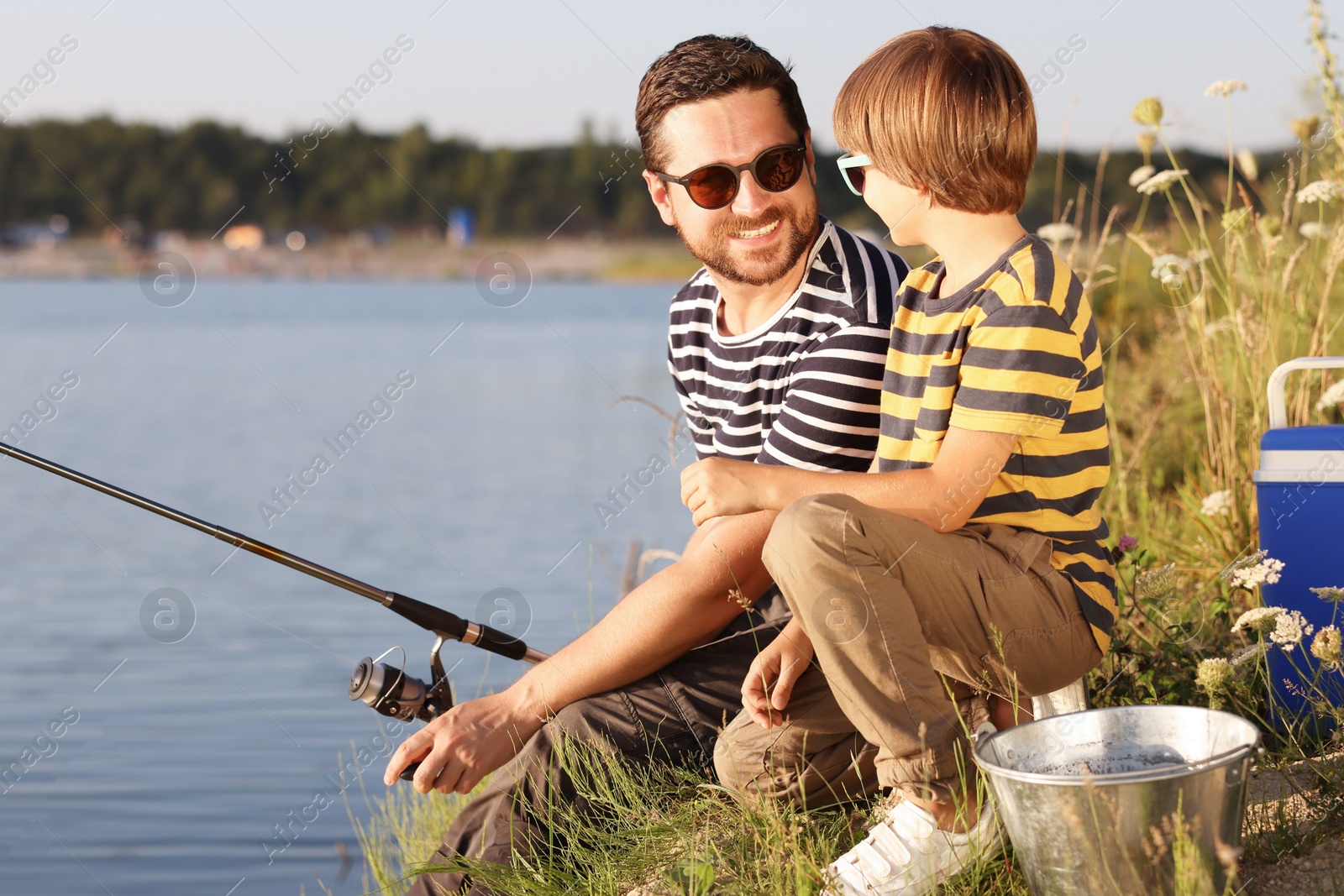 Happy father and his little son in sunglasses fishing together near river outdoors Photo of Happy father and his little son in sunglasses fishing together near river outdoors