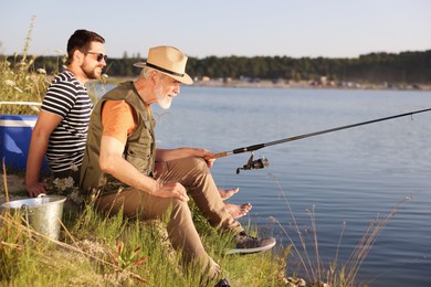 Photo of Elderly father and his happy son fishing together near river outdoors