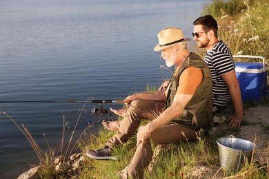 Photo of Elderly father and his happy son fishing together near river outdoors