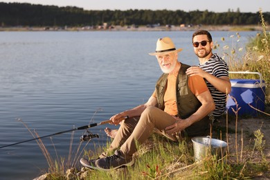 Photo of Elderly father and his happy son fishing together near river outdoors