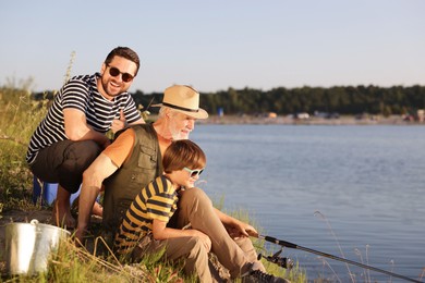 Photo of Smiling grandfather, father and his little son fishing together near river outdoors