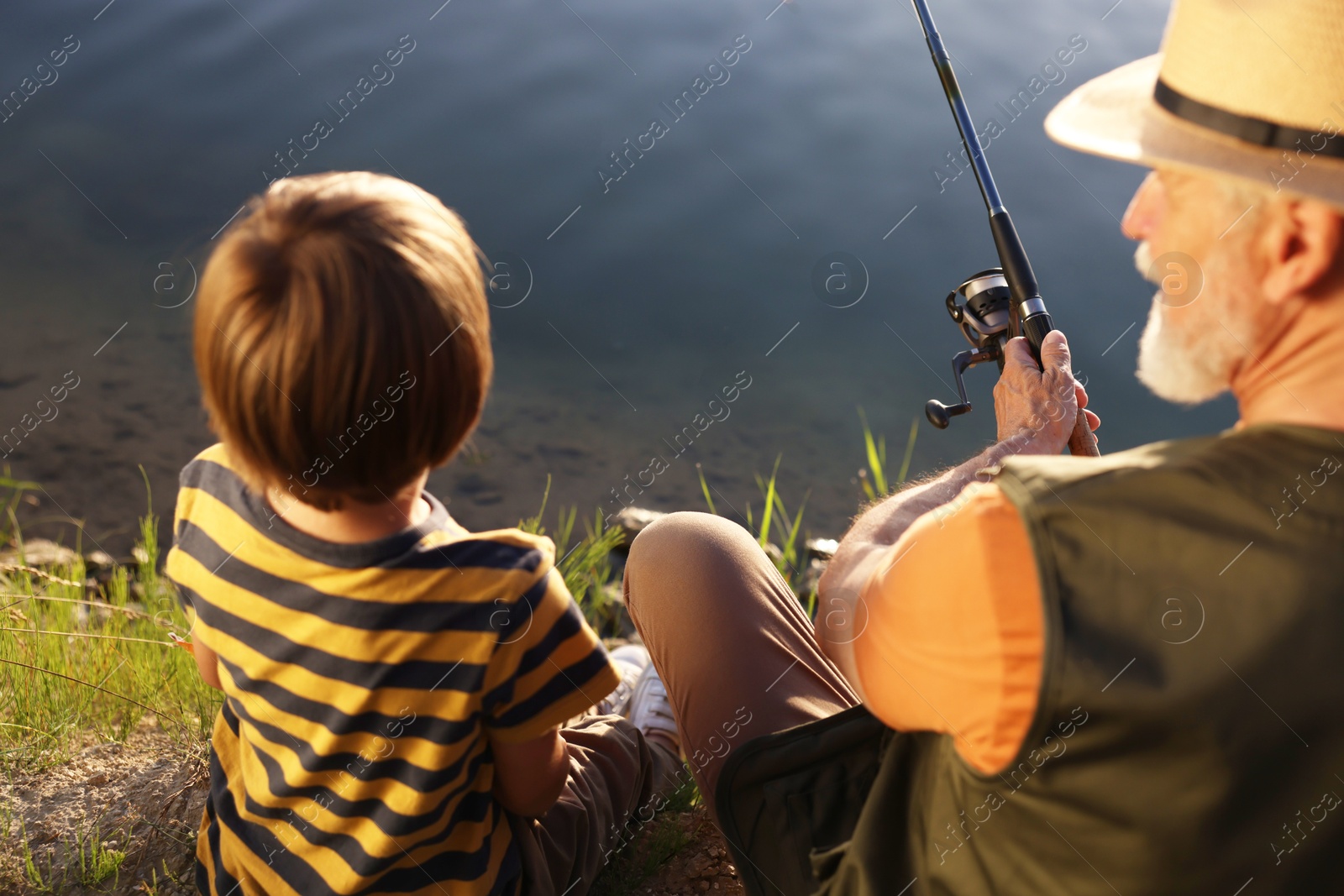 Grandfather and his nephew fishing together near river outdoors, back view Photo of Grandfather and his nephew fishing together near river outdoors, back view